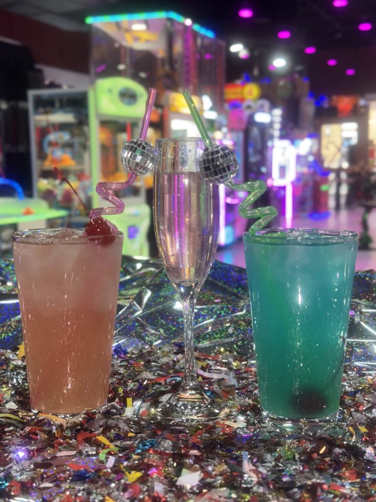 Three colorful drinks served on a sparkly table inside the arcade